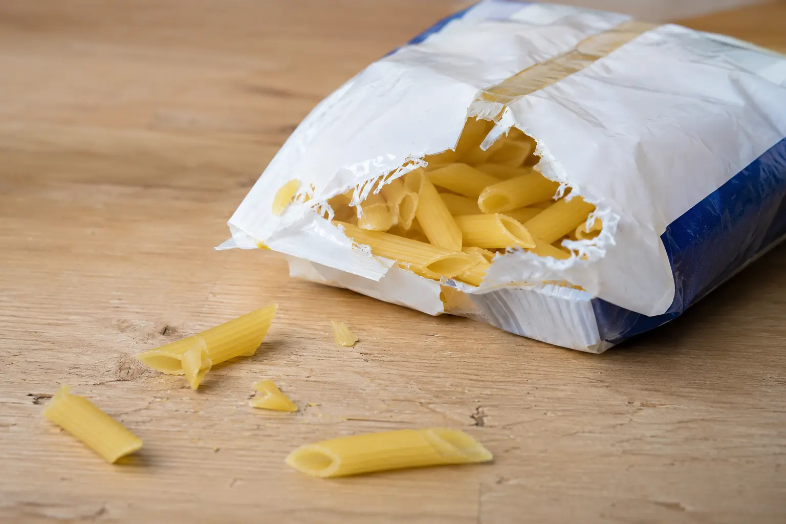 Aufgerissene Nudelverpackung mit Nagespur auf einer Holzfläche